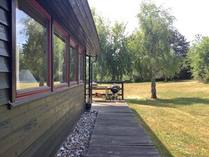 Eine Holzterrasse führt zu einer überdachten Veranda mit Grill und Tisch.