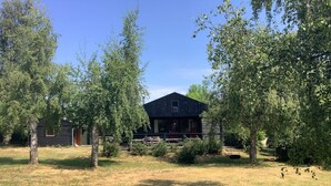 A rustic cabin with a dark wooden exterior, surrounded by a grassy yard and trees.
