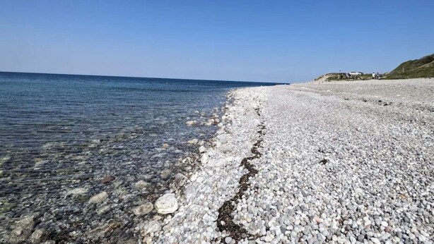 A pebbled beach with clear water and a distant shoreline.