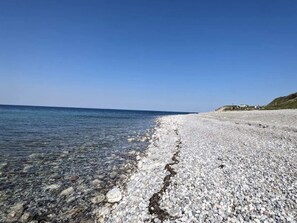 Ein Kiesstrand mit klarem Wasser und einer fernen Küste.
