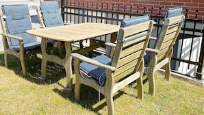 A wooden outdoor table and chairs with blue cushions, set against a brick wall with a metal fence. - 6 Person Holiday Home in Solvesborg (Sölvesborg)