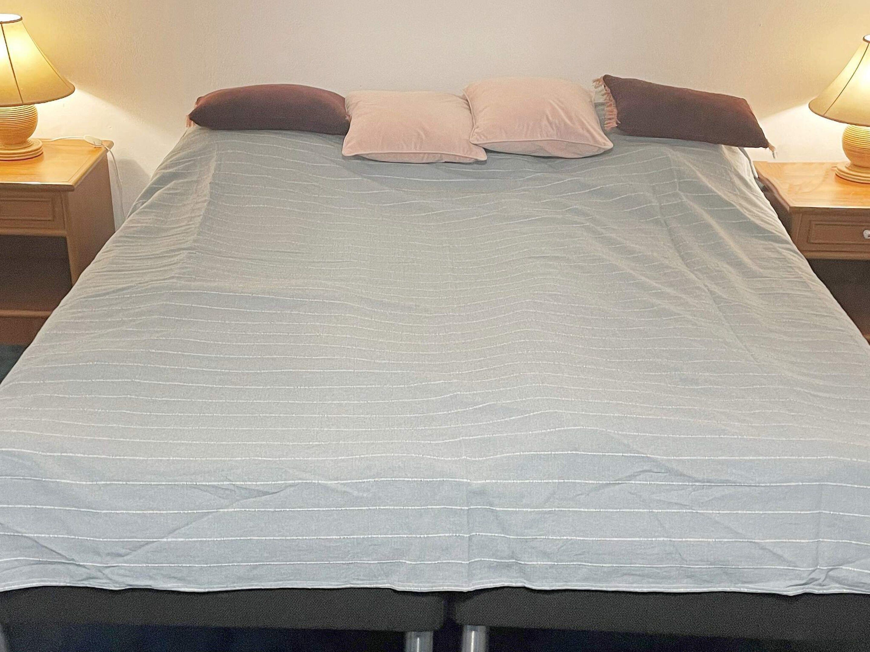 Sänky valkoisella päiväpeitteellä, kaksi yöpöytää, joissa on lamput, ja kaksi tyynyä.