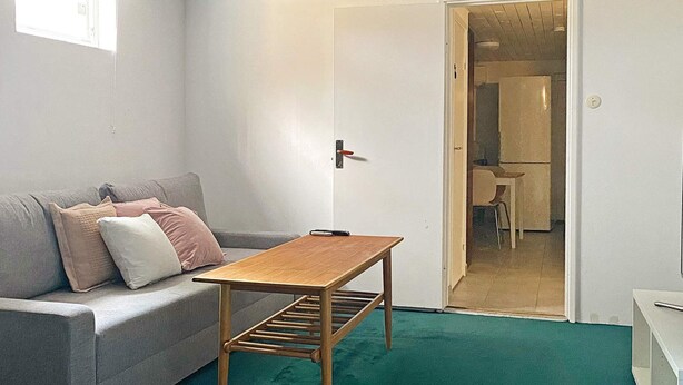 A room with a grey sofa, a wooden table, and a teal carpet. - 6 Person Holiday Home in Solvesborg (Sölvesborg)