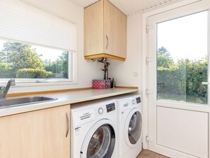 A compact kitchen with a washing machine, a sink, and a window overlooking greenery. - 6 Person Holiday Home in Karrebaeksminde (Karrebæksminde)