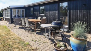 Un patio con mobiliario exterior, una parrilla y una planta en maceta.