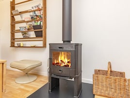 Una habitación con una estufa de leña, una cesta de mimbre y una silla.