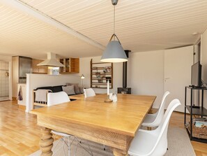 A modern living space with a wooden dining table, white chairs, a kitchen area with cabinets, a built-in bookshelf, and a ceiling with linear lighting. - 6 Person Holiday Home in Karrebaeksminde (Karrebæksminde)