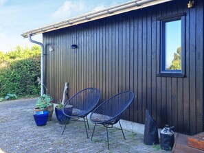 A building with a dark wooden exterior, a window, and two metal chairs outside. - 6 Person Holiday Home in Karrebaeksminde (Karrebæksminde)