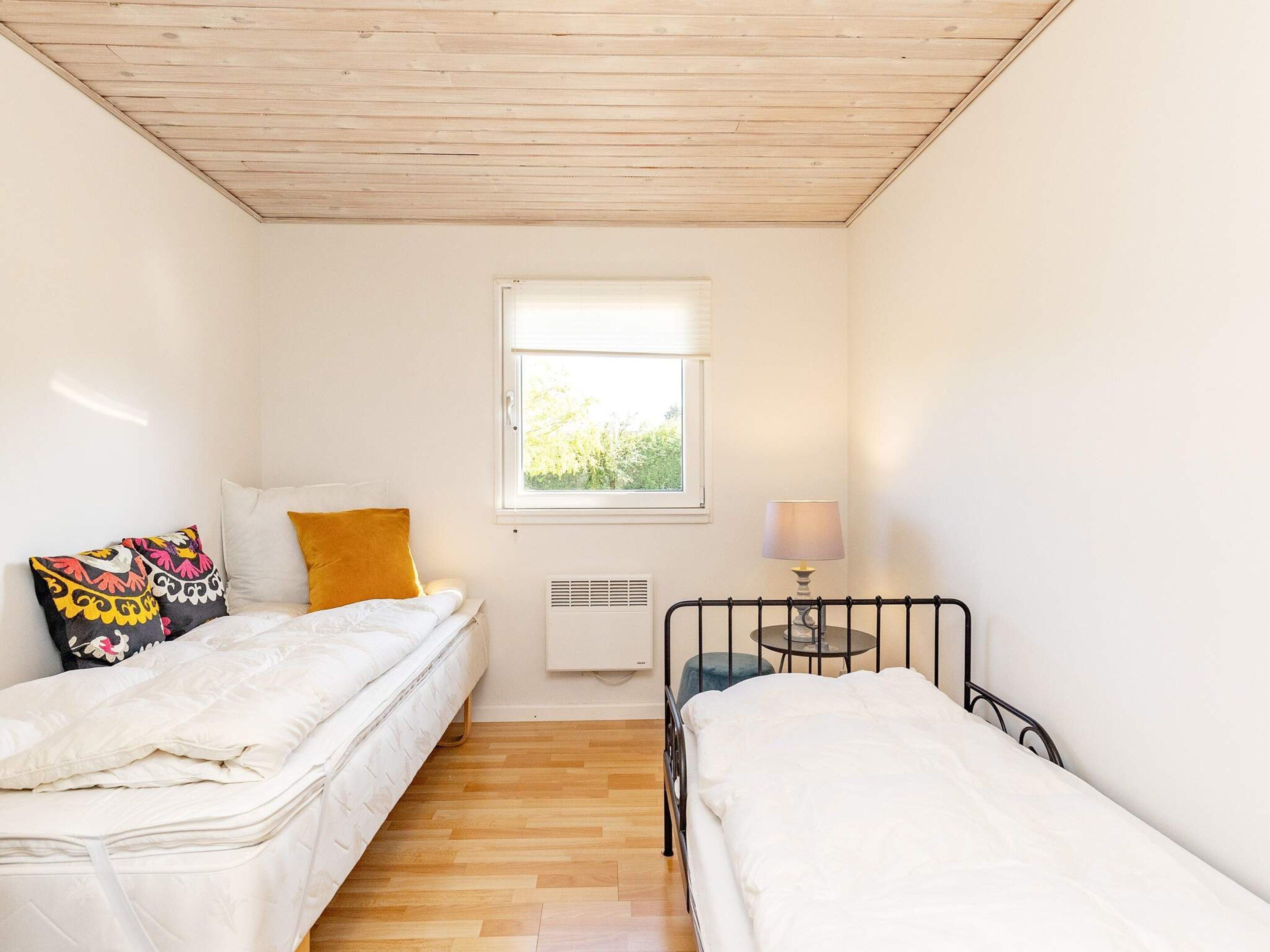 Een eenvoudige, eenpersoonskamer met twee bedden, een raam, een radiator en een tafel met een lamp.