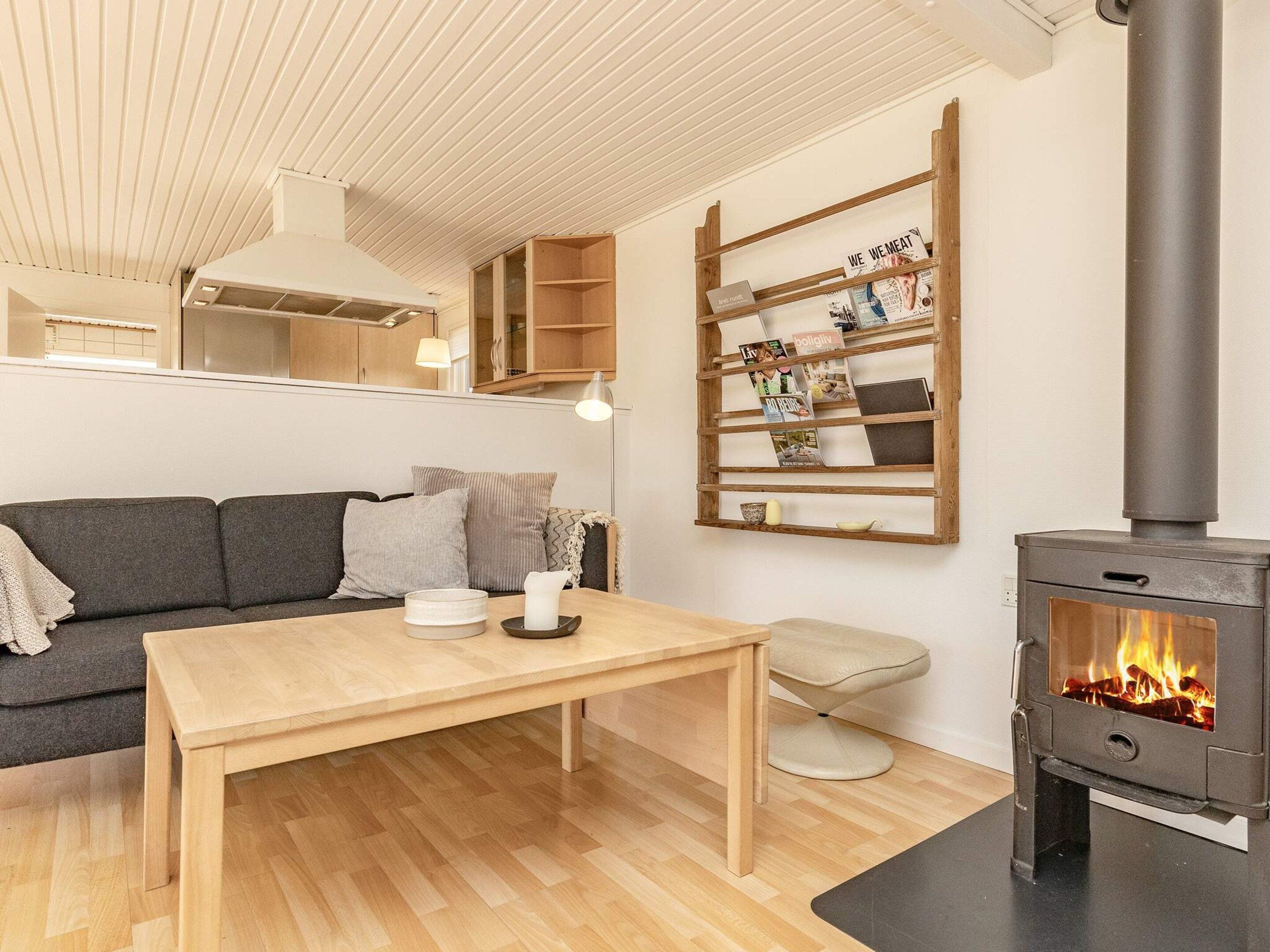 Een gezellige woonkamer met een bank, een houten tafel, een open haard en een wandplank met tijdschriften.