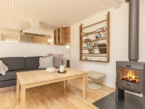 A cozy living room with a sofa, a wooden table, a fireplace, and a wall-mounted shelf with magazines. - 6 Person Holiday Home in Karrebaeksminde (Karrebæksminde)