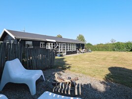 Un edificio de madera con patio cercado, una fogata y mobiliario exterior.