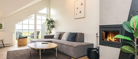 Ein modernes Wohnzimmer mit einer Couch, einem Couchtisch, einem Kamin und einem großen Fenster.