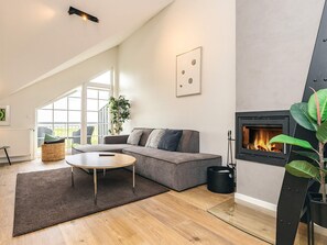 A modern living room with a grey sofa, a round coffee table, a fireplace, and a large window. - 8 Person Holiday Home in Bogense (Bogense)