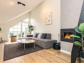 Una sala moderna con un sofá gris, una mesa de centro redonda, una chimenea y un ventanal amplio.