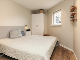 Un dormitorio con una cama, un armario, una mesita y una ventana.