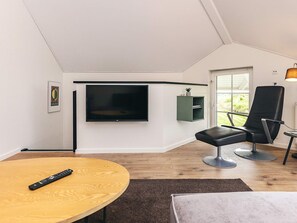 A modern living room with a flat-screen TV, a black leather chair, a wooden table, and a small green shelf. - 8 Person Holiday Home in Bogense (Bogense)