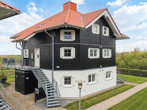 A two-story building with a red-tiled roof, a staircase leading to a balcony, and a small outdoor area with a metal railing. - 8 Person Holiday Home in Bogense (Bogense)