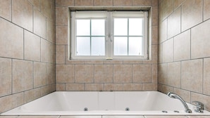 Un baño con bañera, ventana y paredes con azulejos.
