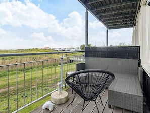 A balcony with wicker furniture, a stone planter, and a view of a marina. - 8 Person Holiday Home in Bogense (Bogense)