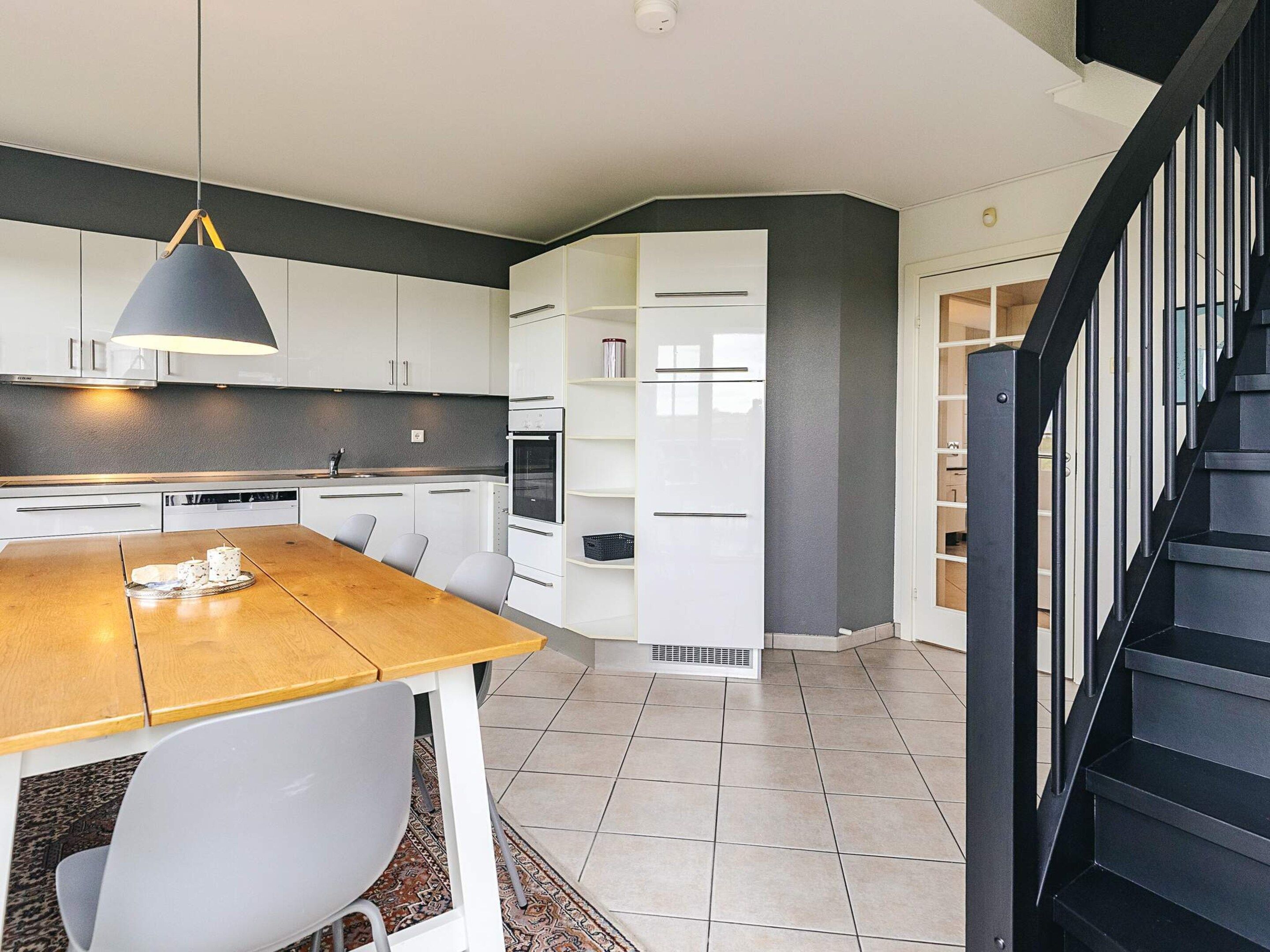 Una cocina moderna con armarios blancos, una mesa de comedor de madera y una escalera negra.