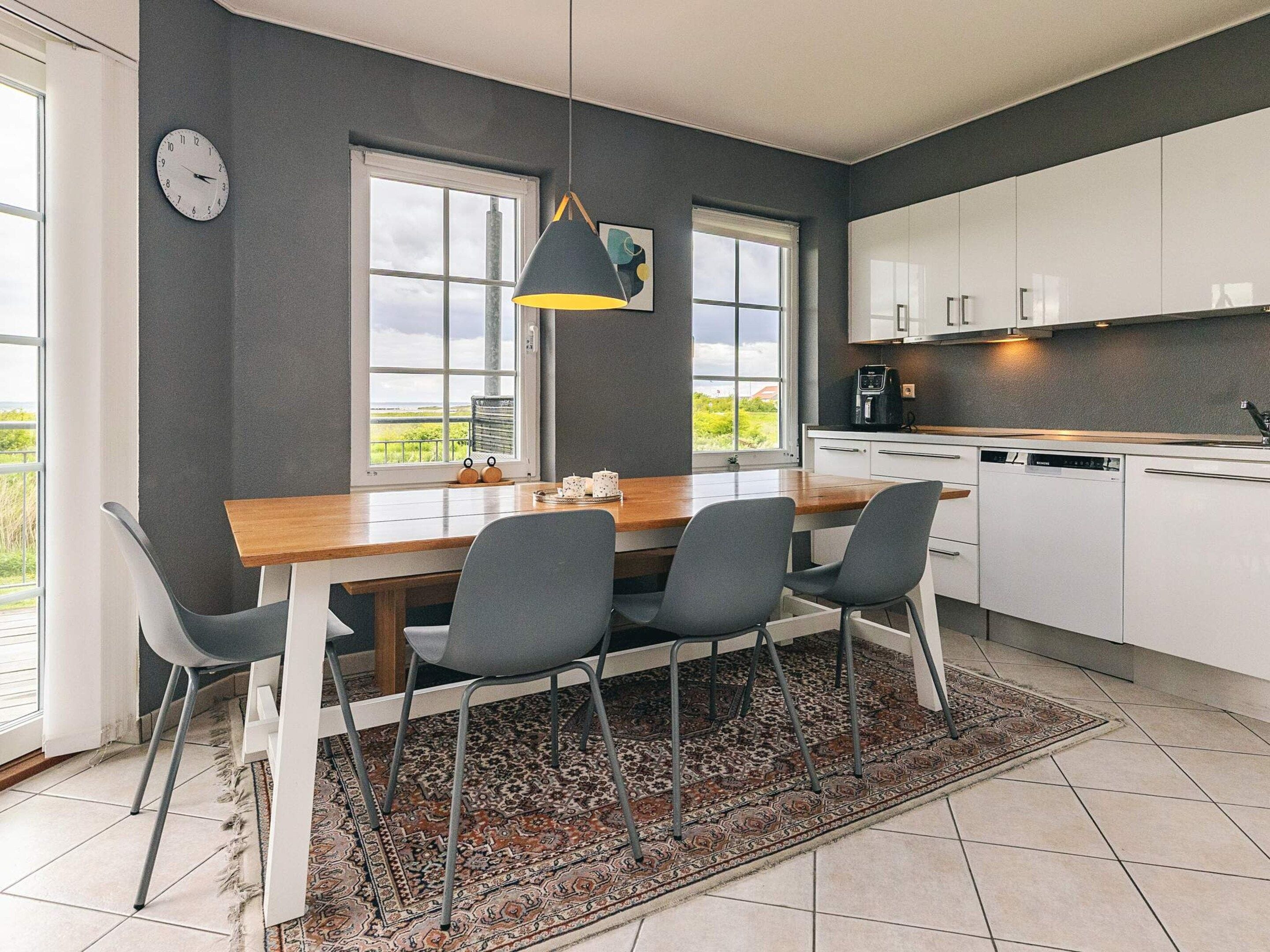 Eine moderne Küche mit einem Holztisch, vier Stühlen, einem Teppich und Blick ins Freie durch große Fenster.