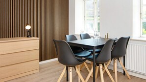 A modern dining area with a wooden panel wall, a round table with six chairs, and a small desk with a lamp. - 6 Person Holiday Home in Sydals (Sydals)