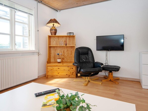 A living room with a wooden cabinet, a black leather chair, a TV on the wall, and a radiator. - 4 Person Holiday Home in Sydals (Sydals)