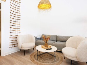 Una sala de estar moderna con un sofá, dos sillones, una mesa redonda de centro y una lámpara colgante.