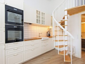 A kitchen with white cabinets, a black oven, a wooden countertop, and a white spiral staircase.