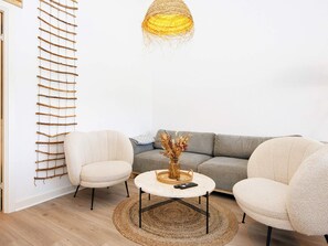 A living room with a sofa, two armchairs, a round coffee table, a woven wall hanging, and a hanging light fixture.