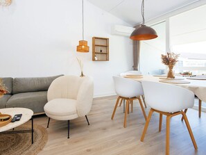 A modern living room with a grey sofa, a white armchair, and a dining area with a table and chairs. - 8 Person Holiday Home in Ringkobing (Ringkobing)