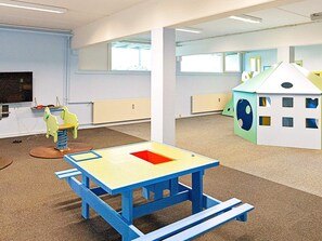 Una sala de juegos con una mesa azul, un caballo de juguete y una casita.