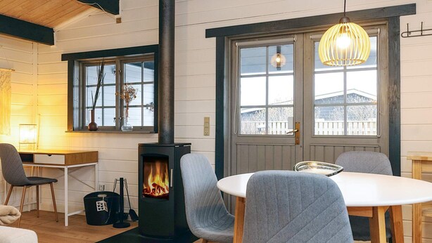 A cozy room with a wood-burning stove, a dining table with chairs, and a large window with a view of a snowy landscape. - 4 Person Holiday Home in Karrebaeksminde-by Traum (Karrebæksminde)