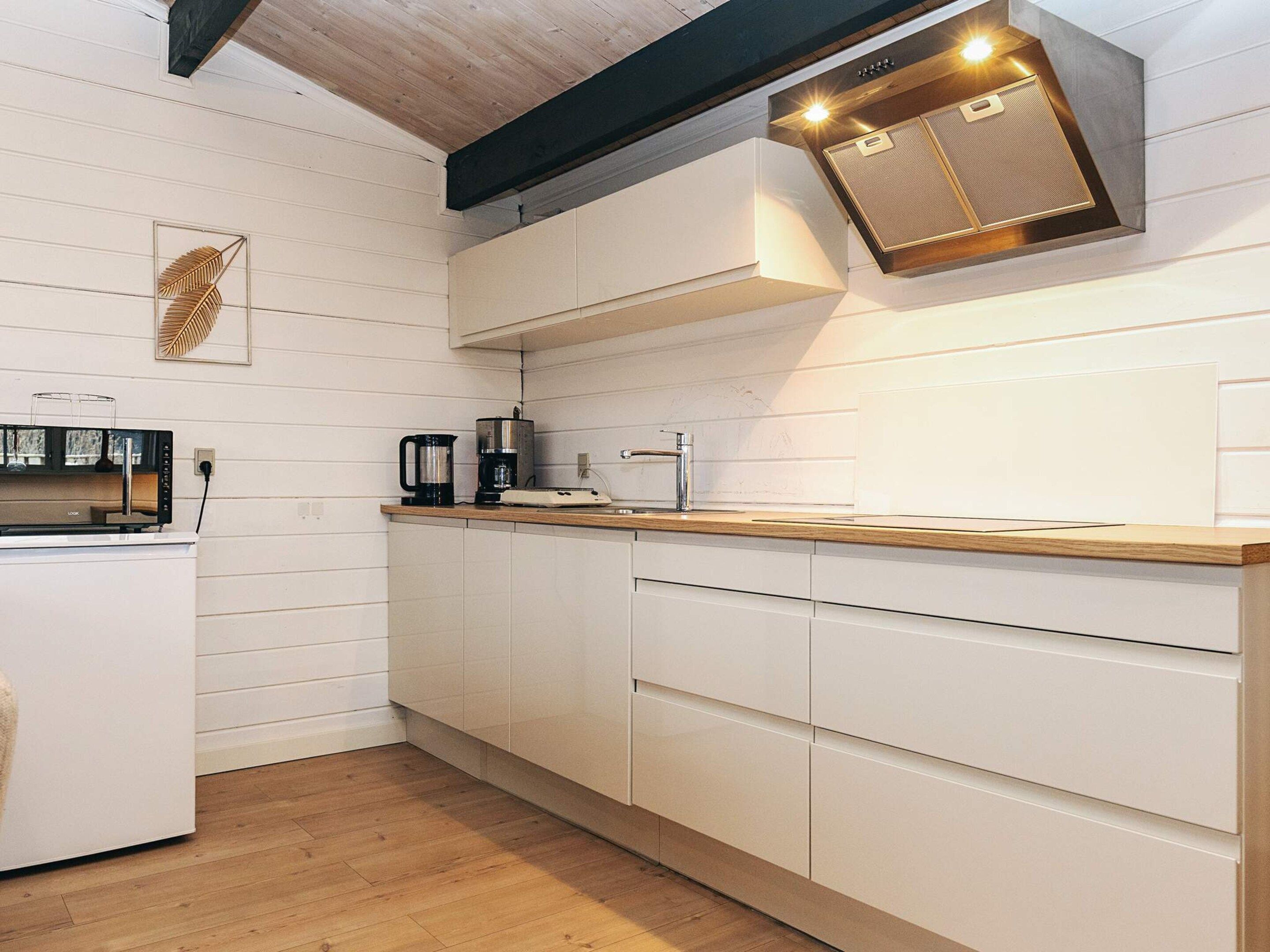 A modern kitchen with white cabinetry, a wooden countertop, and a built-in range hood.