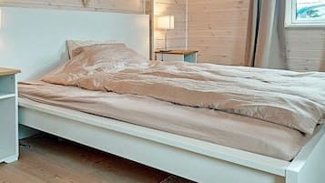 A single-bed room with a wooden headboard, a bedside table, a lamp, and a view of the outdoors through a window.
