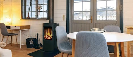 A cozy room with a wood-burning stove, a dining table with chairs, and a large window with a view.