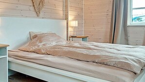A bed with a white frame and a beige bedspread in a room with wooden walls and a window. - 4 Person Holiday Home in Karrebaeksminde-by Traum (Karrebæksminde)
