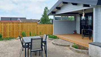 Een terras buiten met een tafel en stoelen, een houten terras en een overdekt gedeelte met een stoel.