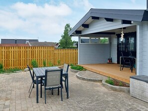 Um pátio externo com mesa e cadeiras, um deck de madeira e uma área coberta com uma poltrona.
