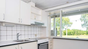 Et moderne køkken med hvide skabe, en rustfri stålvask, indbygget ovn og et vindue med udsigt til grøn natur.