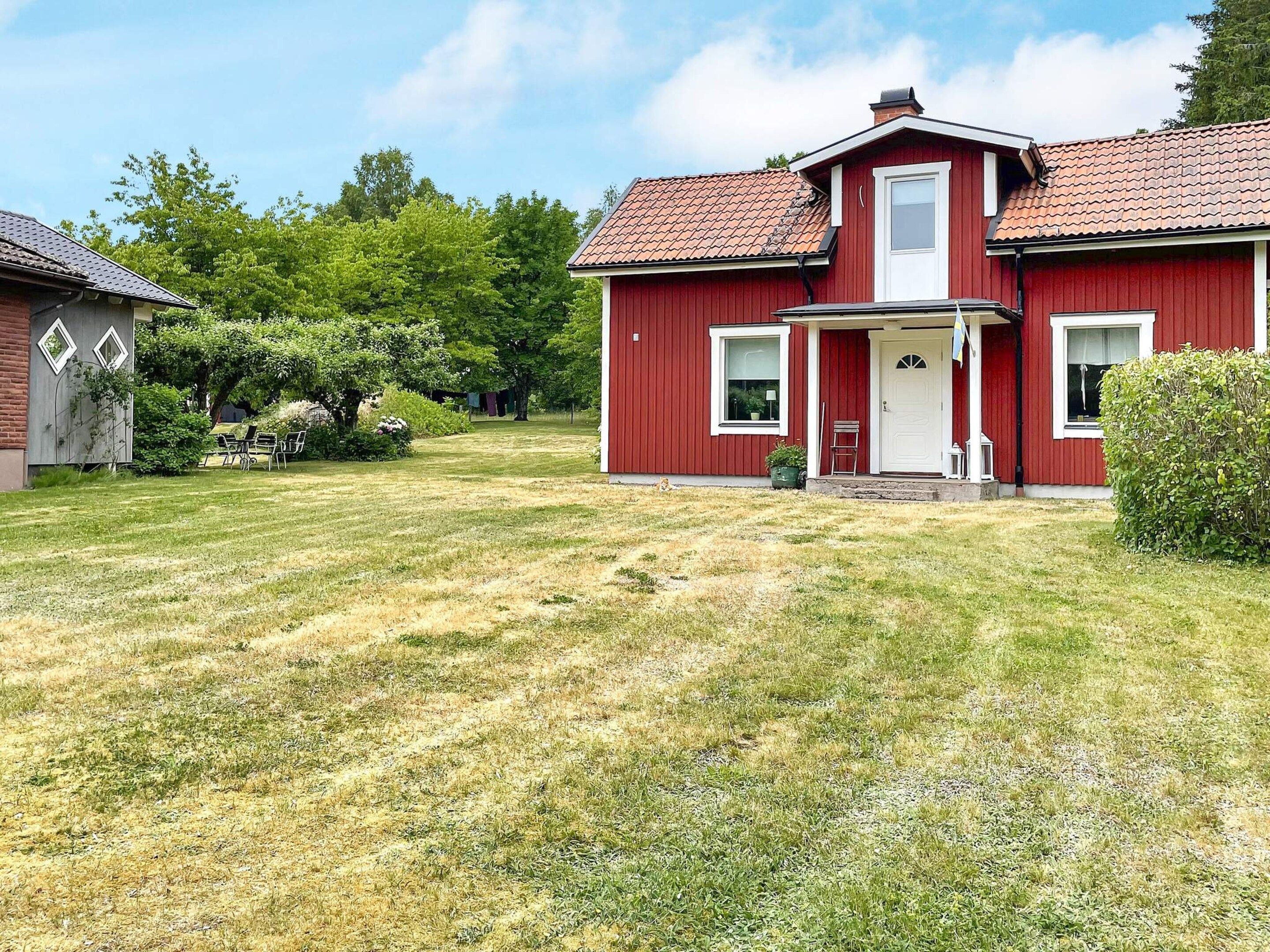 A red two-story house with a front porch, a small garden, and a lawn.