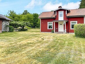 Une maison rouge à deux étages, avec un porche à l’avant, un petit jardin et une pelouse.