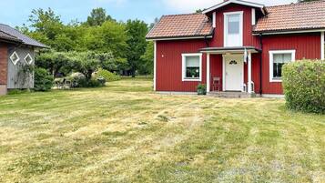 A red house with a front porch, a lawn, and a tree in the background.
