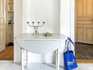A white table with a candelabra and a small decorative item on top, a blue bag with text beside it, and a door leading to a room with a tiled floor. - 7 Person Holiday Home in Motala (Motala)
