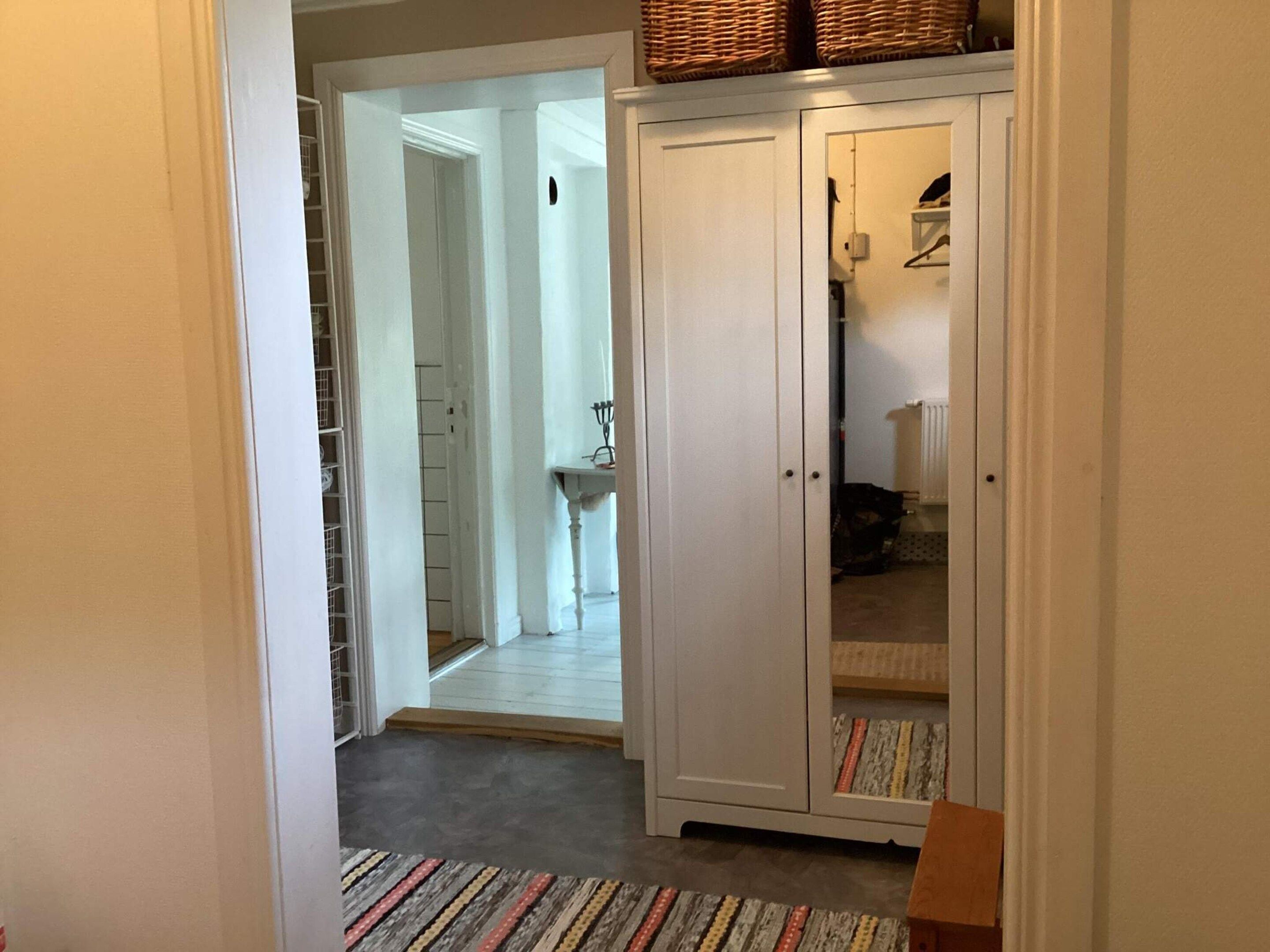 A hallway with a white wardrobe, a patterned rug, and a glimpse of a dining area.