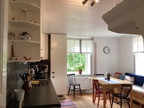 A kitchen with a dining area, a clock on the wall, and a window with a view of greenery. - 7 Person Holiday Home in Motala (Motala)