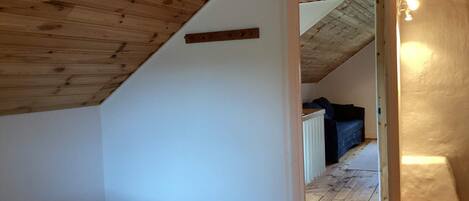 A room with a sloped ceiling, a wooden door leading to another room, and a white wall.