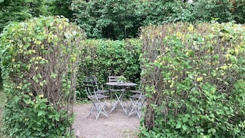 A garden with a metal table and chairs, surrounded by dense foliage.