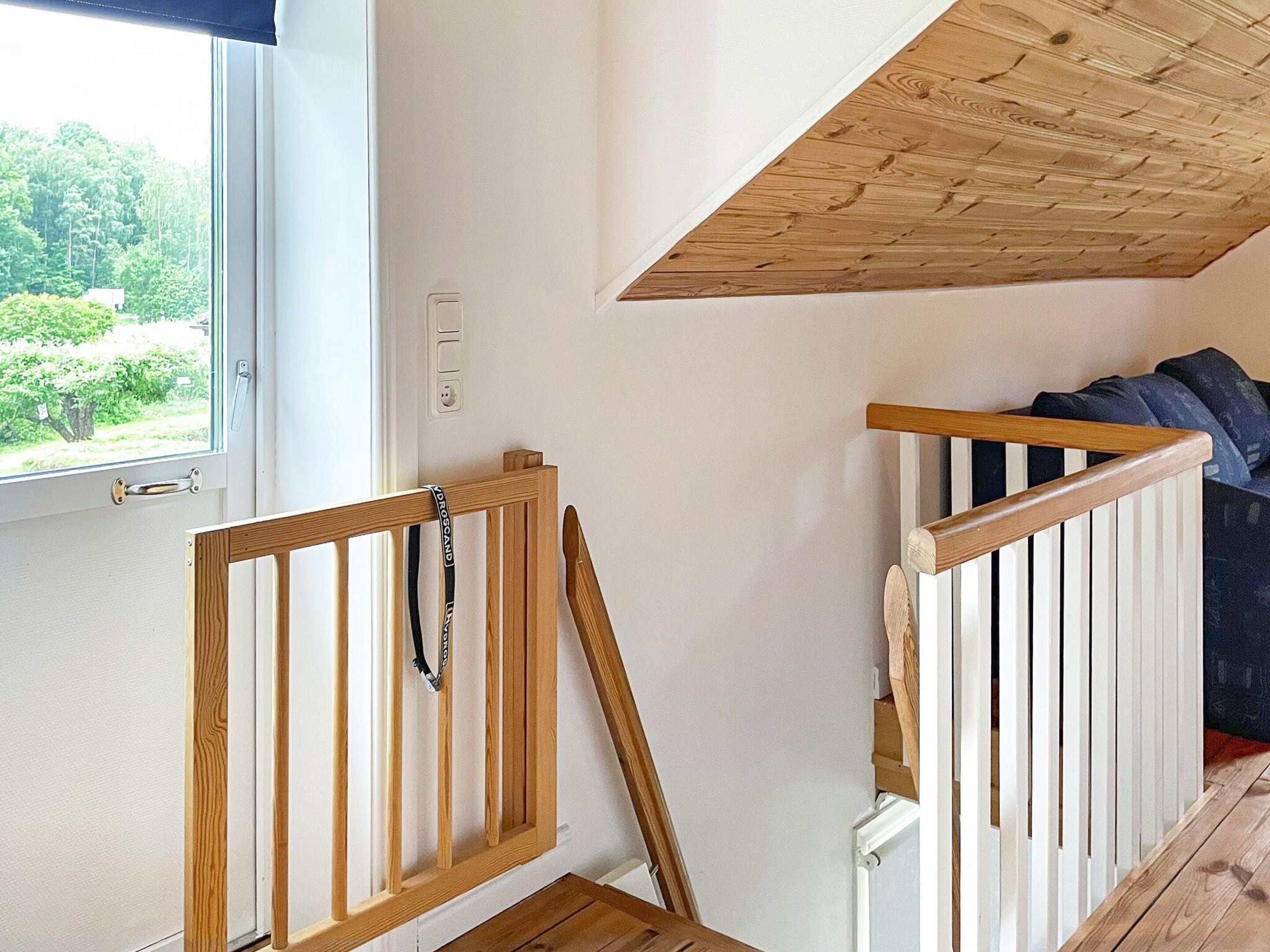 A room with a wooden staircase, a window with a view of greenery, and a white wall.